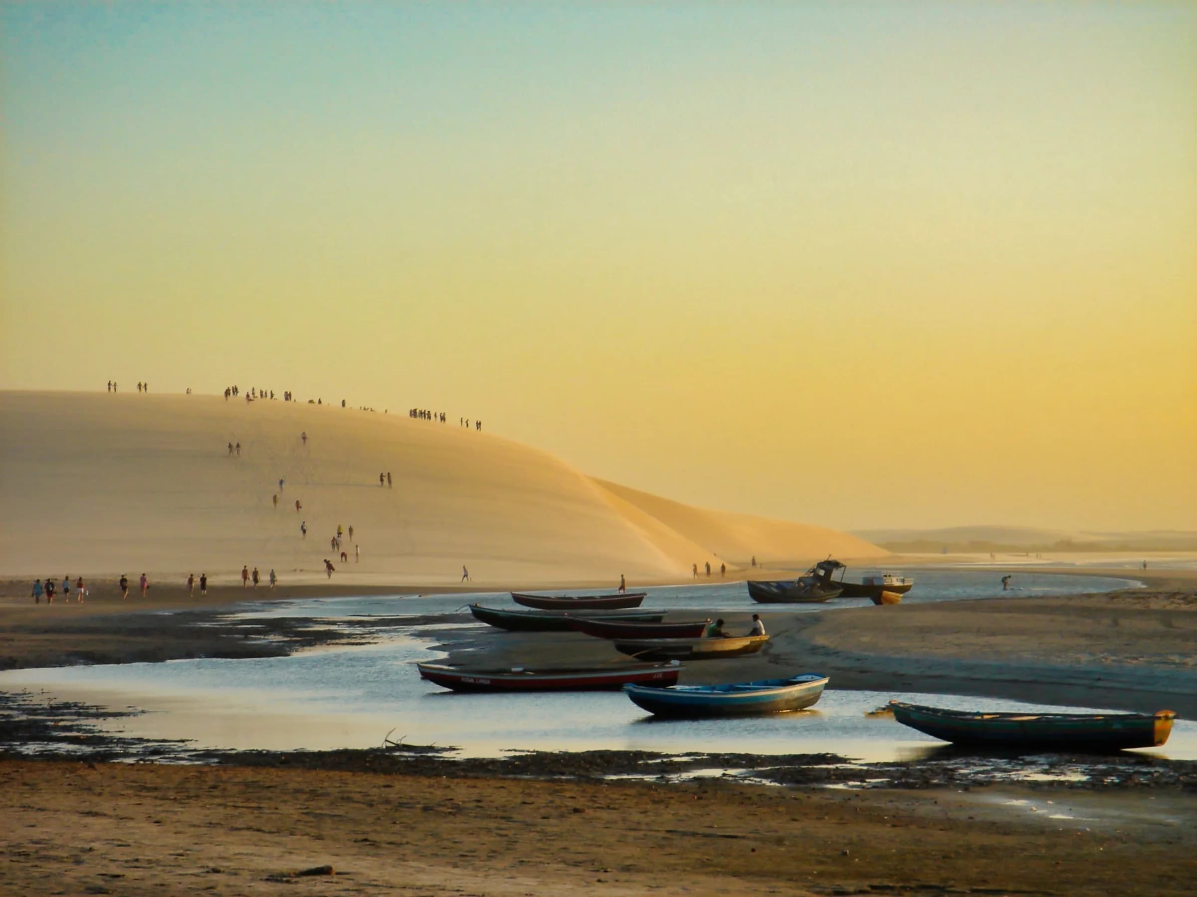 Bateaux au pied d’une grande dune de Jericoacoara au coucher du soleil.
