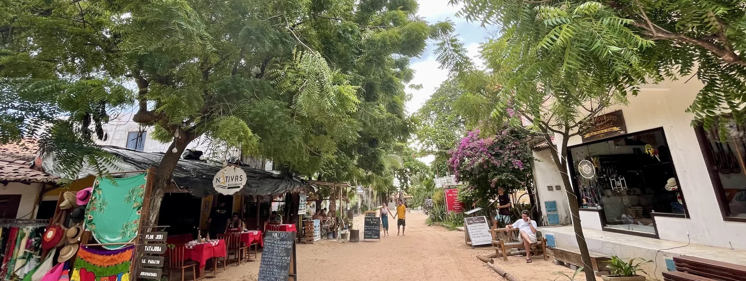 Rue sablonneuse bordée de commerces et de végétation dans le village de Jericoacoara.